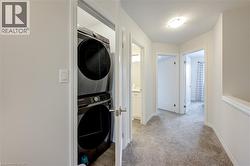 Laundry area with light colored carpet, stacked washer and clothes dryer, and a textured ceiling -