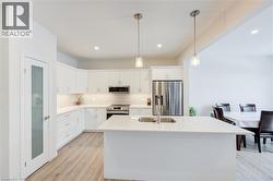 Kitchen with backsplash, decorative light fixtures, white cabinetry, an island with sink, and stainless steel appliances -
