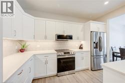 Kitchen featuring stainless steel appliances, white cabinetry, backsplash, light wood-style floors, and light stone countertops -