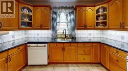 Kitchen featuring glass insert cabinets, brown cabinetry, white dishwasher, and dark stone counters -