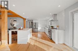 Kitchen with white cabinets, appliances with stainless steel finishes, wall chimney range hood, a kitchen bar, and light wood finished floors -