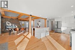 Kitchen featuring white cabinets, stainless steel appliances, light wood finished floors, beamed ceiling, and light stone counters -