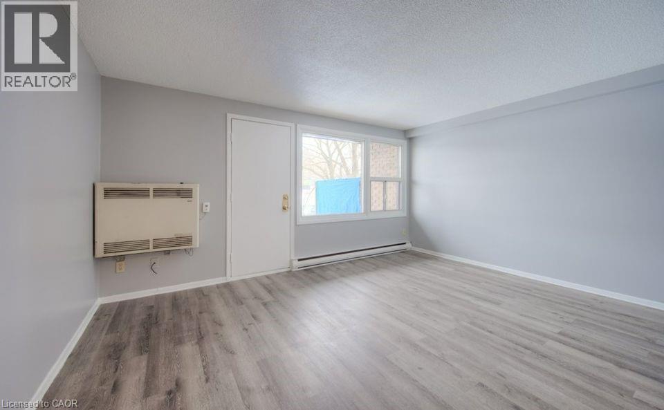 Spare room with a textured ceiling, light wood finished floors, heating unit, and a baseboard radiator - 1200 Courtland Avenue E Unit# 25, Kitchener, ON - Indoor Photo Showing Other Room