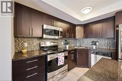 Kitchen featuring stainless steel appliances, backsplash, dark brown cabinets, light tile patterned floors, and dark stone counters -