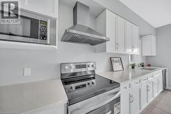 Kitchen featuring appliances with stainless steel finishes, wall chimney exhaust hood, white cabinetry, and light stone countertops -