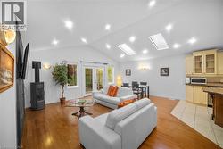Living area featuring a skylight, light wood finished floors, vaulted ceiling, french doors, and a wood stove -