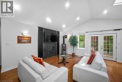Living room featuring vaulted ceiling, a wood stove, wood finished floors, recessed lighting, and french doors -