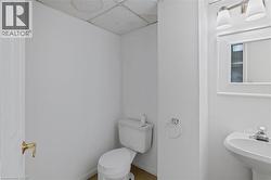 Half bath with a drop ceiling, toilet, a sink, and baseboards -