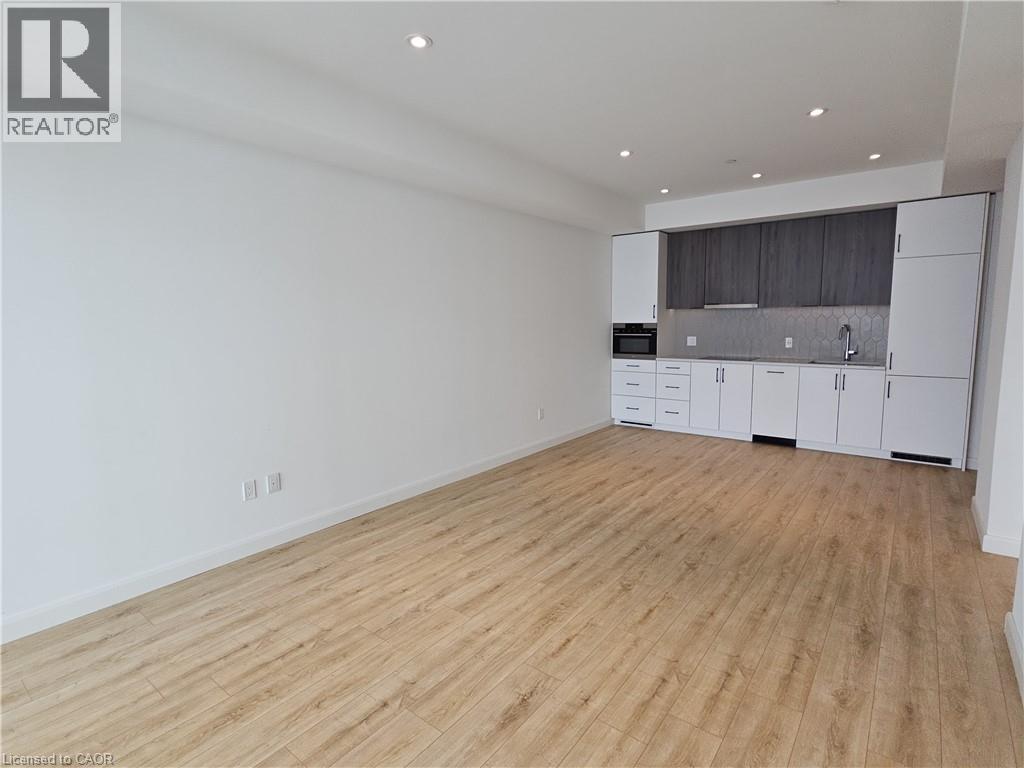 Kitchen featuring tasteful backsplash, modern cabinets, open floor plan, dark brown cabinets, and light wood-type flooring - 741 King Street W Unit# 1207, Kitchener, ON - Indoor Photo Showing Other Room