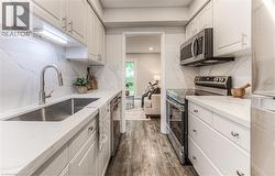 Kitchen featuring appliances with stainless steel finishes, a sink, dark wood-style floors, white cabinetry, and light stone countertops -
