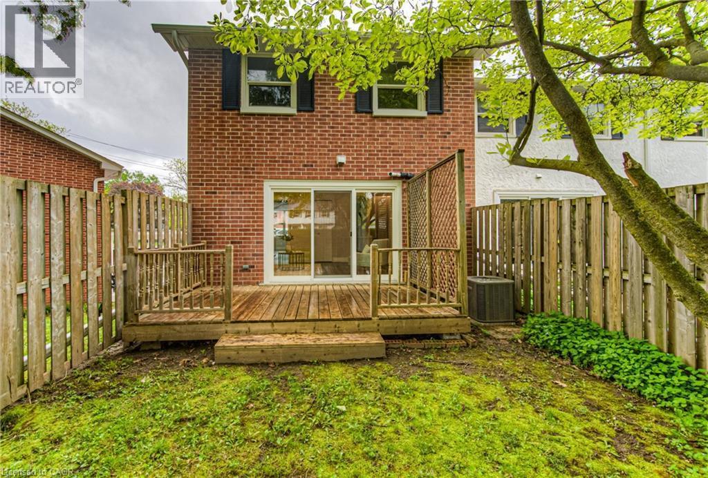 Back of house featuring a fenced backyard, brick siding, central AC, and a deck - 425 Keats Way Unit# 4, Waterloo, ON - Outdoor With Deck Patio Veranda