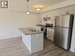 Kitchen with stainless steel appliances, dark wood-style floors, pendant lighting, under cabinet range hood, and white cabinetry -