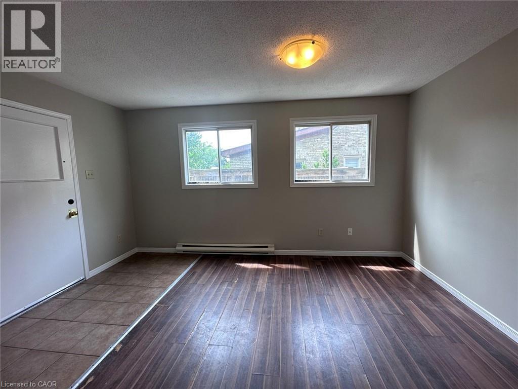 Unfurnished room featuring a textured ceiling, hardwood / wood-style floors, and a baseboard radiator - 17 St Leger Street, Kitchener, ON - Indoor Photo Showing Other Room