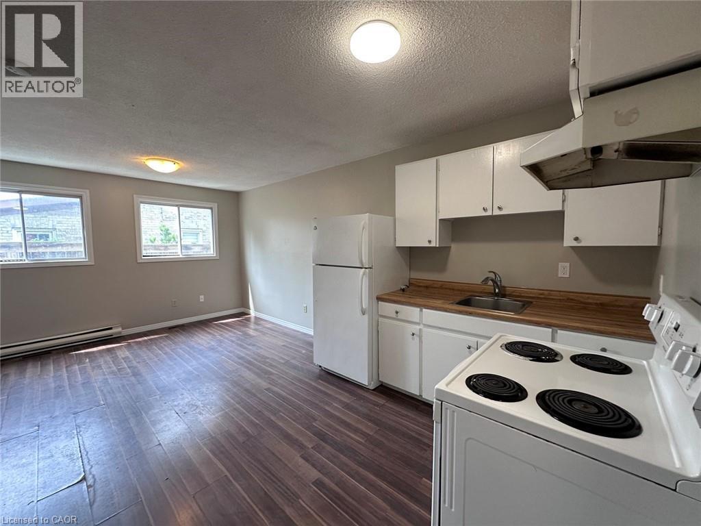 Kitchen featuring white appliances, white cabinets, a textured ceiling, under cabinet range hood, and dark wood-type flooring - 17 St Leger Street, Kitchener, ON - Indoor Photo Showing Kitchen