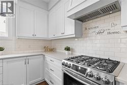Kitchen with gas range, premium range hood, white cabinetry, and tasteful backsplash -