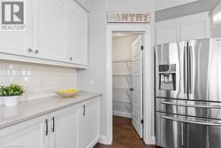 Kitchen featuring stainless steel refrigerator with ice dispenser, white cabinetry, dark wood-type flooring, and light stone countertops -