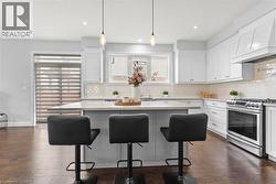 Kitchen featuring gas range, white cabinets, decorative light fixtures, a kitchen island, and custom range hood -