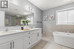 Bathroom with a stall shower, double vanity, light tile patterned floors, tile walls, and a freestanding tub -