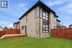 Back of property with a fenced backyard, a gate, a deck, and stone siding -