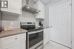 Kitchen featuring stainless steel electric stove, wall chimney range hood, white cabinetry, and light tile patterned floors -