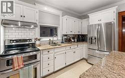 Kitchen with appliances with stainless steel finishes, light stone countertops, backsplash, white cabinets, and ornamental molding -