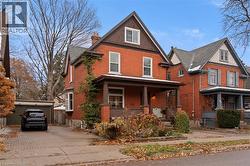 View of front facade featuring an outbuilding, brick siding, covered porch, and a chimney -
