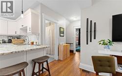 Kitchen featuring light stone countertops, light wood finished floors, backsplash, white cabinetry, and hanging light fixtures -