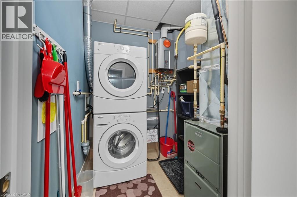Laundry room featuring a paneled ceiling, light tile patterned floors, estacked washer and dryer, heating unit, and tankless water heater - 8111 Forest Glen Drive Unit# 524, Niagara Falls, ON - Indoor Photo Showing Laundry Room