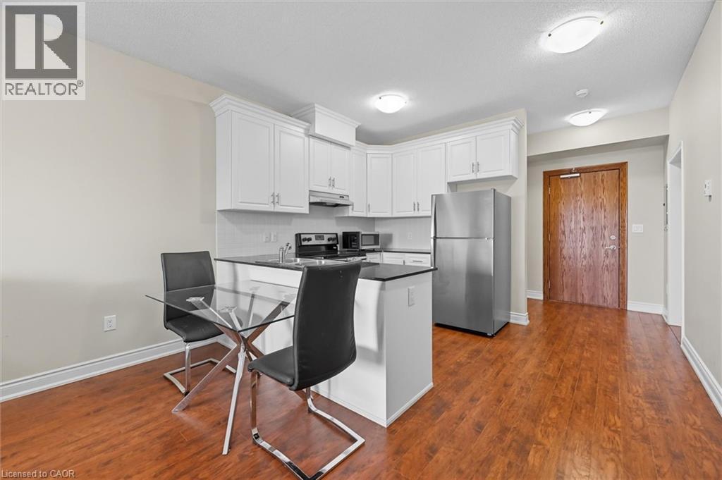 Kitchen with appliances with stainless steel finishes, white cabinets, a peninsula, dark wood-style floors, and a breakfast bar area - 8111 Forest Glen Drive Unit# 524, Niagara Falls, ON - Indoor