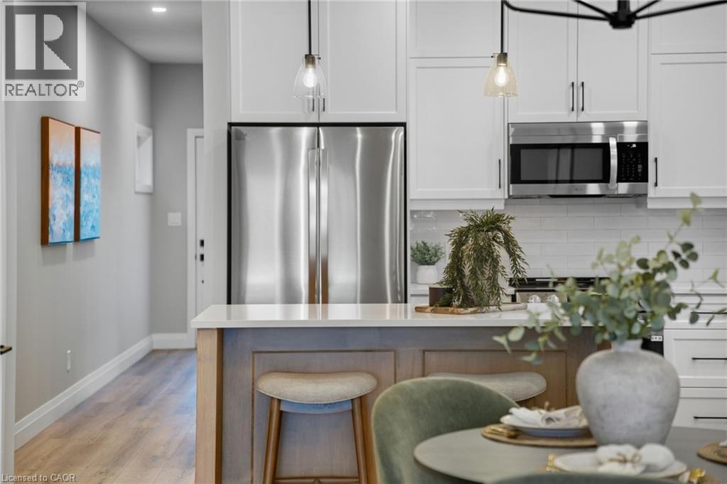 Kitchen with stainless steel appliances, white cabinets, a breakfast bar, decorative backsplash, and light wood-style flooring - 29 Weymouth Street Unit# 17, Elmira, ON - Indoor