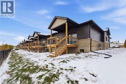 Snow covered house featuring a wooden deck, stairs, and stone siding -