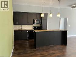 Kitchen featuring hanging light fixtures, tasteful backsplash, black appliances, a center island, and light stone countertops -