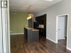 Kitchen with dark cabinets, dark wood-style floors, decorative light fixtures, black appliances, and light stone countertops -