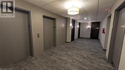 Hallway with elevator, a drop ceiling, and dark carpet -