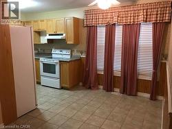 Kitchen with white appliances, dark countertops, under cabinet range hood, ceiling fan, and light tile patterned flooring -