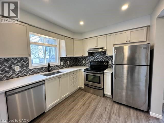 Kitchen featuring stainless steel appliances, light wood-style flooring, under cabinet range hood, decorative backsplash, and recessed lighting - 750 Paris Boulevard Unit# 1, Waterloo, ON - Indoor Photo Showing Kitchen With Stainless Steel Kitchen With Double Sink
