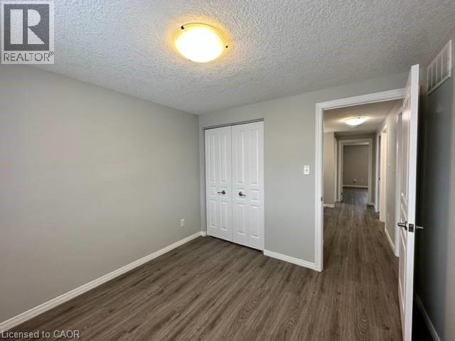 Unfurnished bedroom featuring a textured ceiling, a closet, and dark wood-style flooring - 750 Paris Boulevard Unit# 1, Waterloo, ON - Indoor Photo Showing Other Room