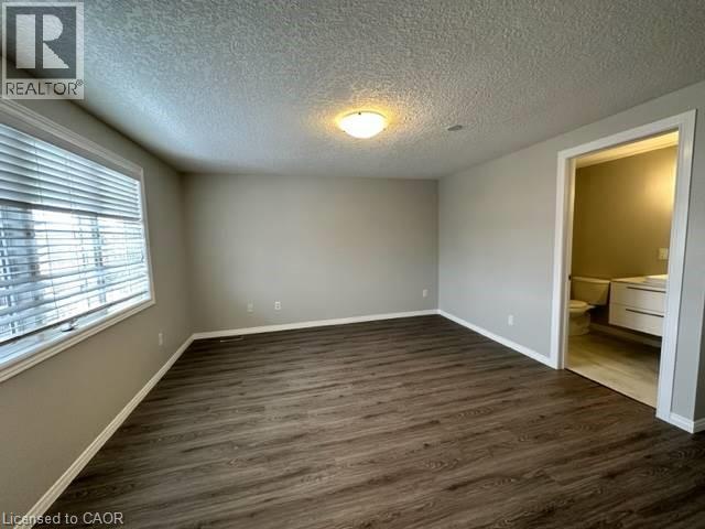Unfurnished bedroom featuring dark wood-type flooring, a textured ceiling, and ensuite bathroom - 750 Paris Boulevard Unit# 1, Waterloo, ON - Indoor Photo Showing Other Room