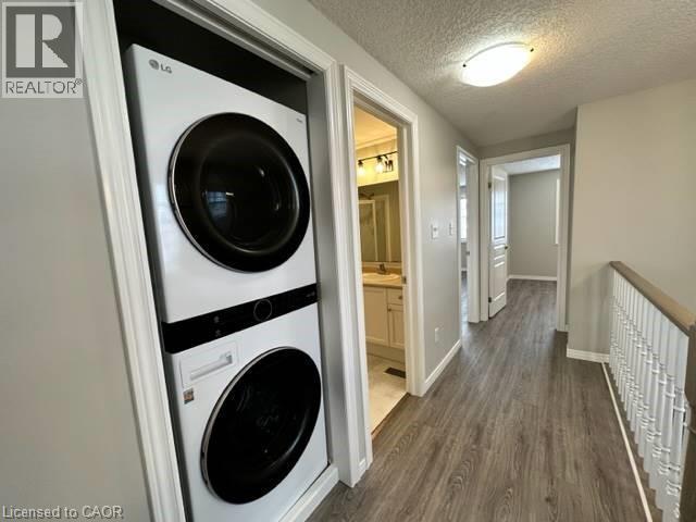 Laundry area featuring a textured ceiling, dark wood-type flooring, and stacked washer and clothes dryer - 750 Paris Boulevard Unit# 1, Waterloo, ON - Indoor Photo Showing Laundry Room