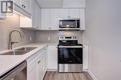 Kitchen with stainless steel appliances, tasteful backsplash, white cabinets, and light stone counters -