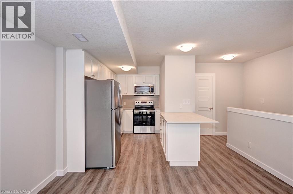 Kitchen featuring stainless steel appliances, white cabinets, a textured ceiling, a peninsula, and light wood-type flooring - 118 Gravel Ridge Trail Unit# C17, Kitchener, ON - Indoor Photo Showing Kitchen With Stainless Steel Kitchen