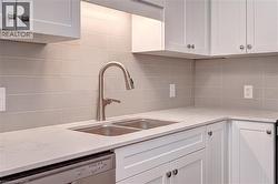 Kitchen with white cabinetry, dishwasher, decorative backsplash, and light stone counters -