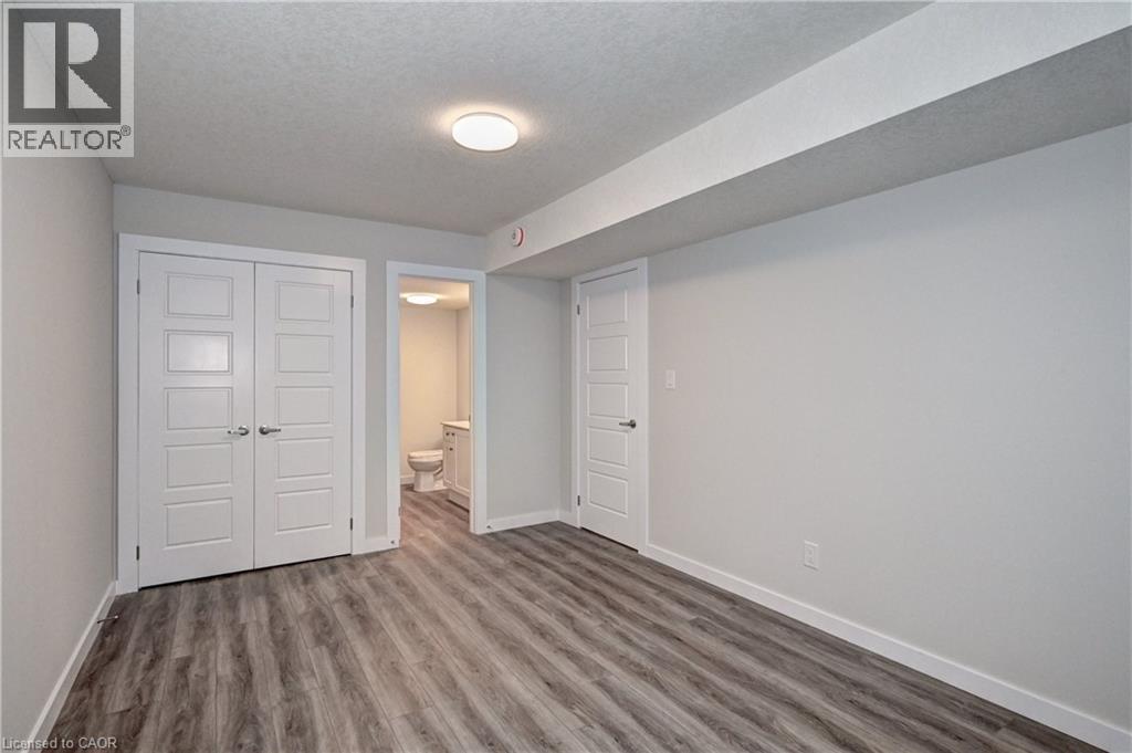 Unfurnished bedroom with wood finished floors, a textured ceiling, a closet, and connected bathroom - 118 Gravel Ridge Trail Unit# G21, Kitchener, ON - Indoor Photo Showing Other Room
