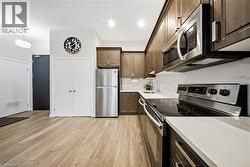 Kitchen featuring stainless steel appliances, light wood-style flooring, pendant lighting, and dark brown cabinetry -