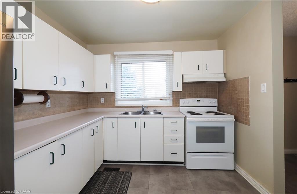 Kitchen featuring white range with electric stovetop, decorative backsplash, light countertops, white cabinetry, and under cabinet range hood - 255 Northlake Drive Unit# 27, Waterloo, ON - Indoor Photo Showing Kitchen With Double Sink