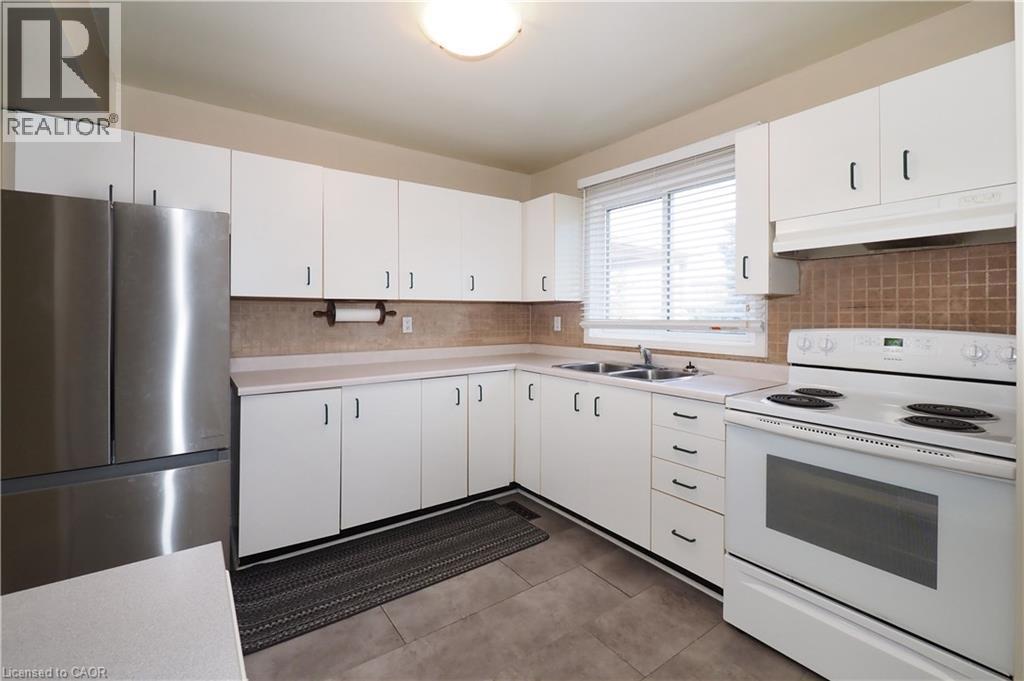 Kitchen featuring white range with electric cooktop, freestanding refrigerator, light countertops, under cabinet range hood, and white cabinetry - 255 Northlake Drive Unit# 27, Waterloo, ON - Indoor Photo Showing Kitchen With Double Sink