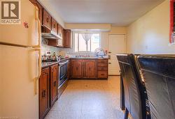 Kitchen with freestanding refrigerator, light floors, electric stove, under cabinet range hood, and dark countertops -