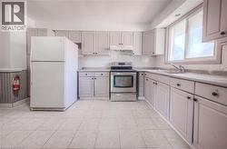 Kitchen featuring stainless steel range with electric cooktop, freestanding refrigerator, light countertops, under cabinet range hood, and a wainscoted wall -