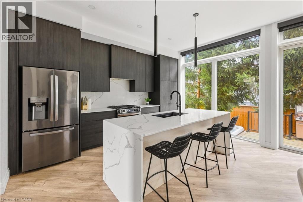 Kitchen featuring floor to ceiling windows, modern cabinets, appliances with stainless steel finishes, a breakfast bar area, and light stone countertops - 26 Huron Street, Grand Bend, ON - Indoor Photo Showing Kitchen With Stainless Steel Kitchen With Double Sink With Upgraded Kitchen