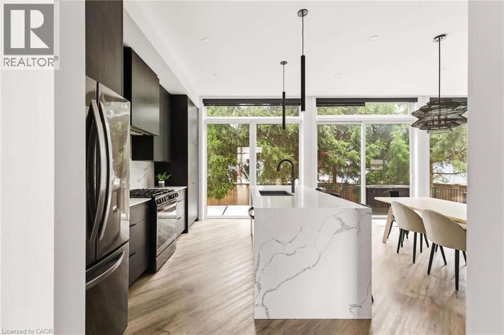 Kitchen featuring expansive windows, modern cabinets, gas range oven, stainless steel refrigerator with ice dispenser, and hanging light fixtures - 26 Huron Street, Grand Bend, ON - Indoor